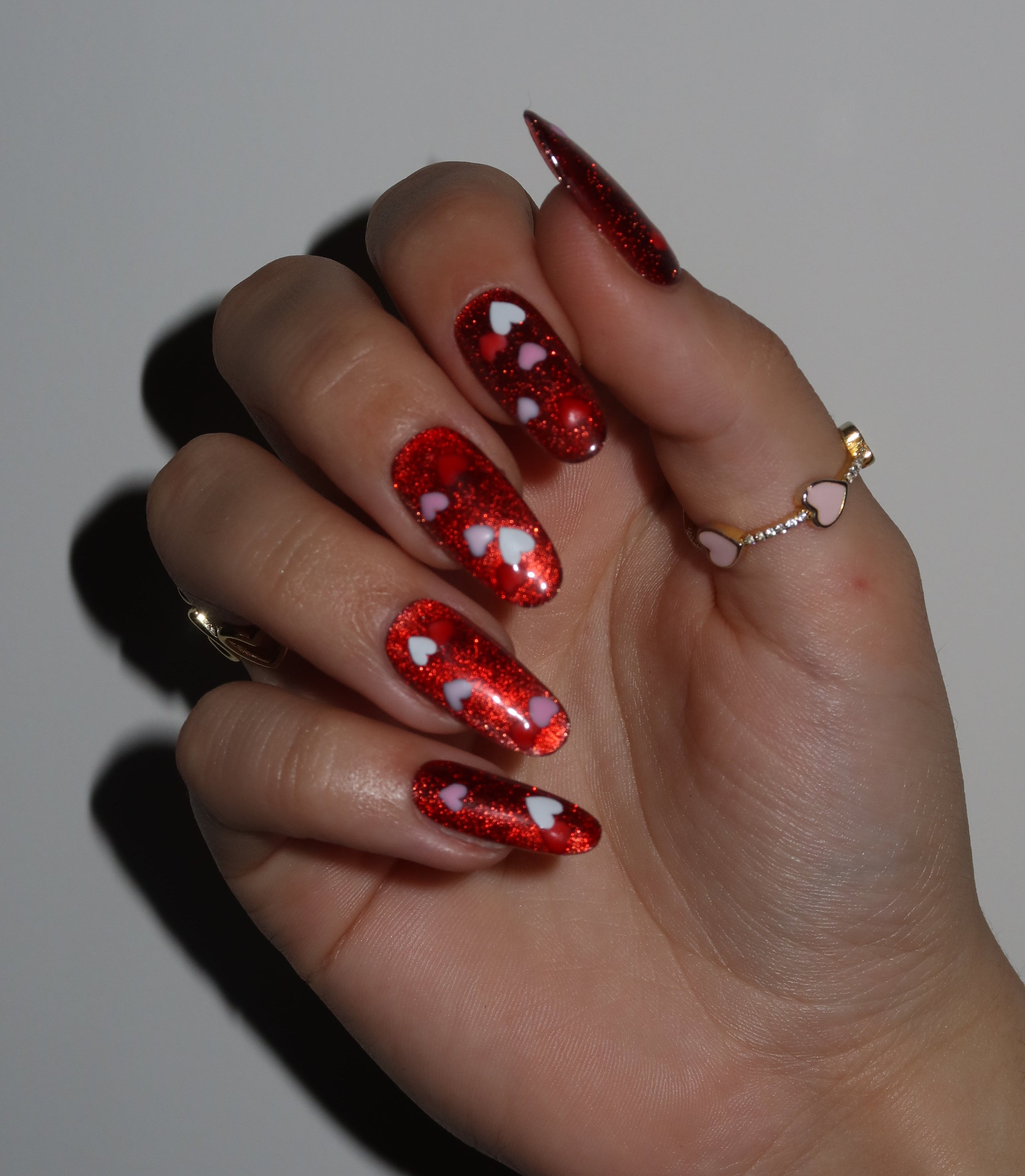 Hand with red glittery nail polish and heart designs on a neutral background